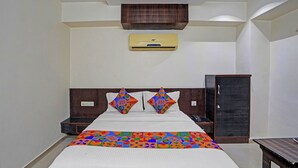 Habitación de hotel con cama, armario, mesita de noche, equipo de aire acondicionado y una pequeña mesa.