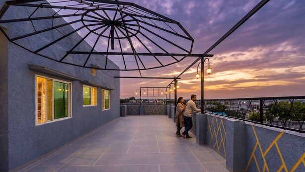 Una terraza en la azotea con una estructura metálica de sombrilla de diseño geométrico, barandillas y vistas a la ciudad al atardecer.
