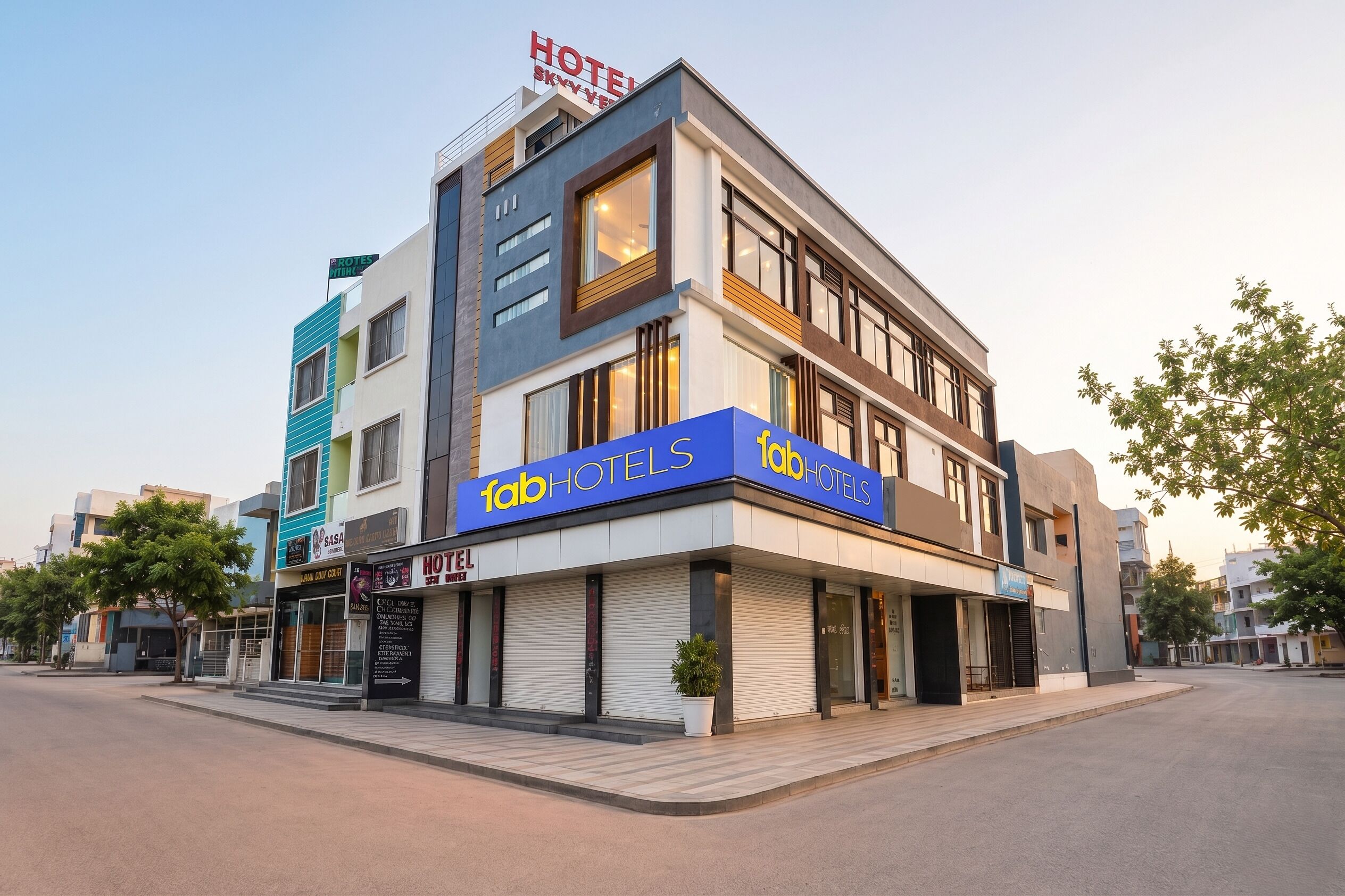 A modern hotel with a prominent 'fabHOTELS' sign, a rooftop sign indicating 'HOTEL SKYVIEW', and a visible entrance with a closed shutter.