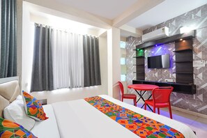 A hotel room with a bed, a TV mounted on the wall, a dining table with chairs, and a window with curtains.
