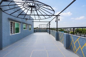 Terraza en la azotea con un muro azul con textura, diseños geométricos de diamantes amarillos y una estructura de sombrilla metálica.