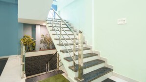 Una escalera con barandilla de vidrio, pared de piedra y un pequeño jardín con plantas.