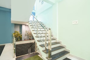 A staircase with a glass railing, a stone wall, and a small garden area with plants.