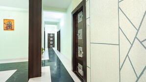 Un pasillo con piso de baldosas, una puerta de madera con un panel de vidrio y una pared con diseño geométrico.