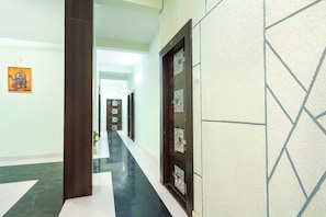 A hallway with a tiled floor, a wooden door with a glass panel, and a wall with a geometric pattern.