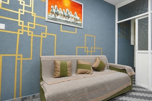 A room with a patterned wall, a sofa with cushions, and a framed picture above the sofa.