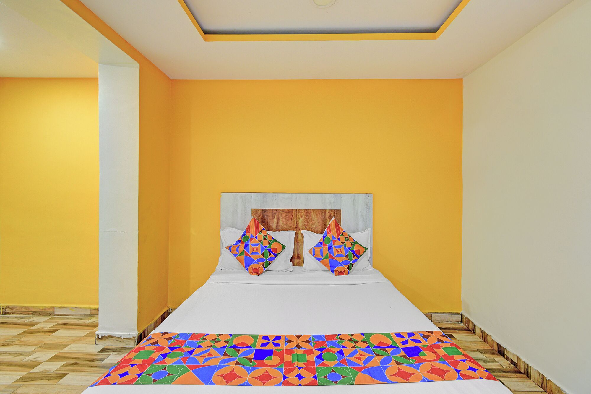 Una habitación con una cama, una pared amarilla y una colcha estampada.