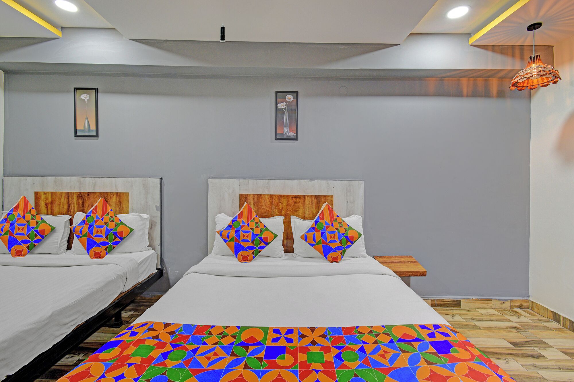 Habitación de hotel con dos camas, cabecera de madera, colcha con estampado geométrico de colores y lámpara colgante.