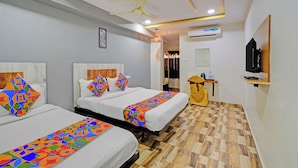 A hotel room with two beds, a ceiling fan, an air conditioning unit, a television, and a wooden floor.
