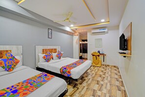 A hotel room with two beds, a ceiling fan, an air conditioning unit, a television, and a wooden floor. - Fabhotel Sri Sai Regency (Hyderabad)