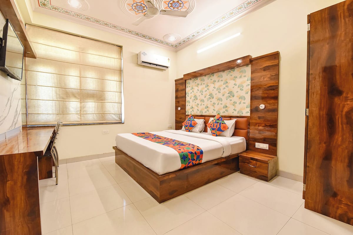 A bedroom with a bed, wooden headboard, bedside tables, and a window with blinds.