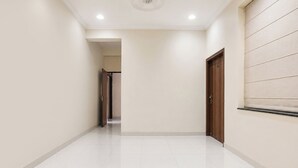 Un pasillo con pisos de baldosas blancas, una puerta de madera a la derecha y una lámpara empotrada en el techo.