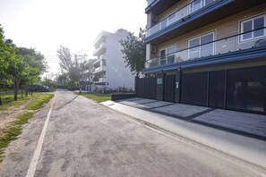 Una calle residencial con edificios de apartamentos, un acceso con portón y una vía despejada.