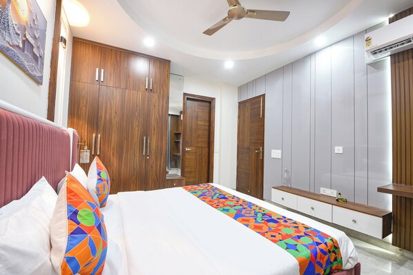 A bedroom with a bed, a ceiling fan, wooden wardrobes, a bedside table, and a wall-mounted air conditioning unit. - Fabhotel The Mamta Grande (Gurugram)