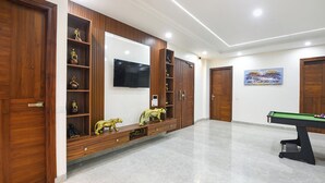 A spacious room with a pool table, wooden cabinets, a flat-screen TV, and a painting on the wall. - Fabhotel The Mamta Grande (Gurugram)
