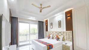 A modern bedroom with a large bed, a ceiling fan, and a view through the window. - Fabhotel The Mamta Grande (Gurugram)