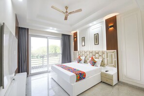 A modern bedroom with a large bed, a ceiling fan, and a view through the window. - Fabhotel The Mamta Grande (Gurugram)