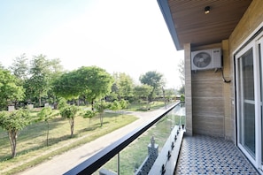A balcony with a view of a park, a tiled floor, and an air conditioning unit. - Fabhotel The Mamta Grande (Gurugram)