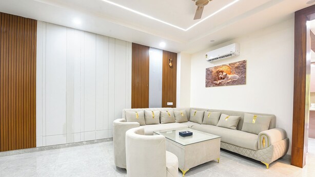 A modern living room with a sectional sofa, a glass coffee table, and a ceiling fan. - Fabhotel The Mamta Grande (Gurugram)
