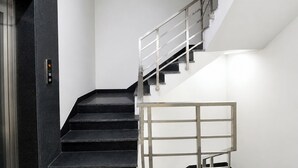 A staircase with a metal railing, a digital elevator control panel, and a white wall. - Fabhotel The Mamta Grande (Gurugram)