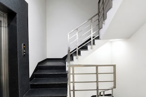 A staircase with a metal railing, a digital elevator control panel, and a white wall. - Fabhotel The Mamta Grande (Gurugram)