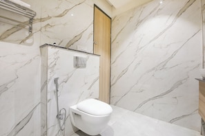 A bathroom with a toilet, shower, and marble walls. - Fabhotel The Rolex Grand (Faridabad)