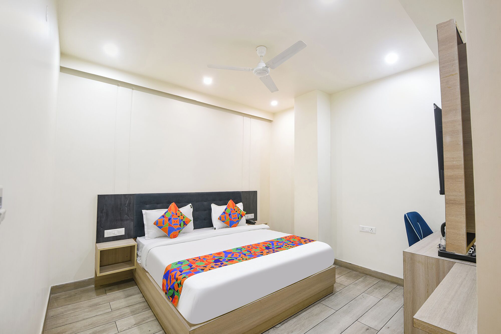A modern bedroom with a bed, a ceiling fan, a bedside table, and a desk with a chair.