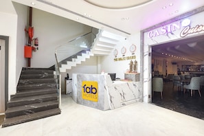 A hotel lobby with a marble reception desk, a staircase, and a casino sign. - Fabhotel The Rolex Grand (Faridabad)