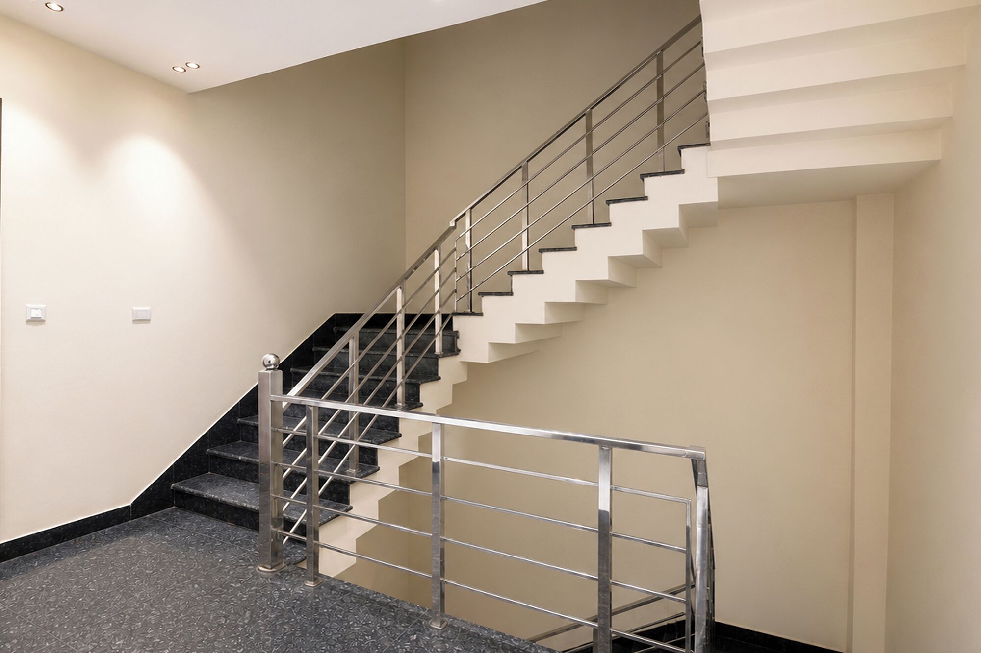 Una escalera moderna con barandilla de metal, paredes color beige y suelo alfombrado.