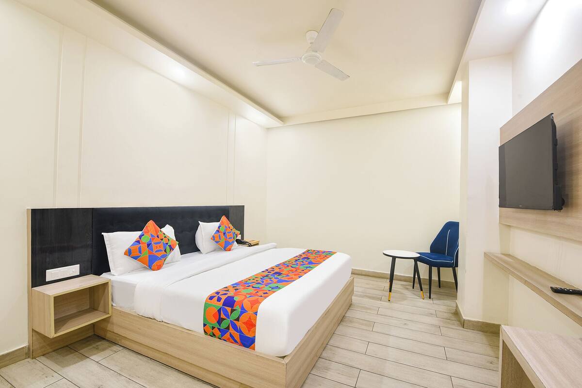 Habitación de hotel con cama, mesita de noche, una silla, televisor montado en la pared y ventilador de techo.