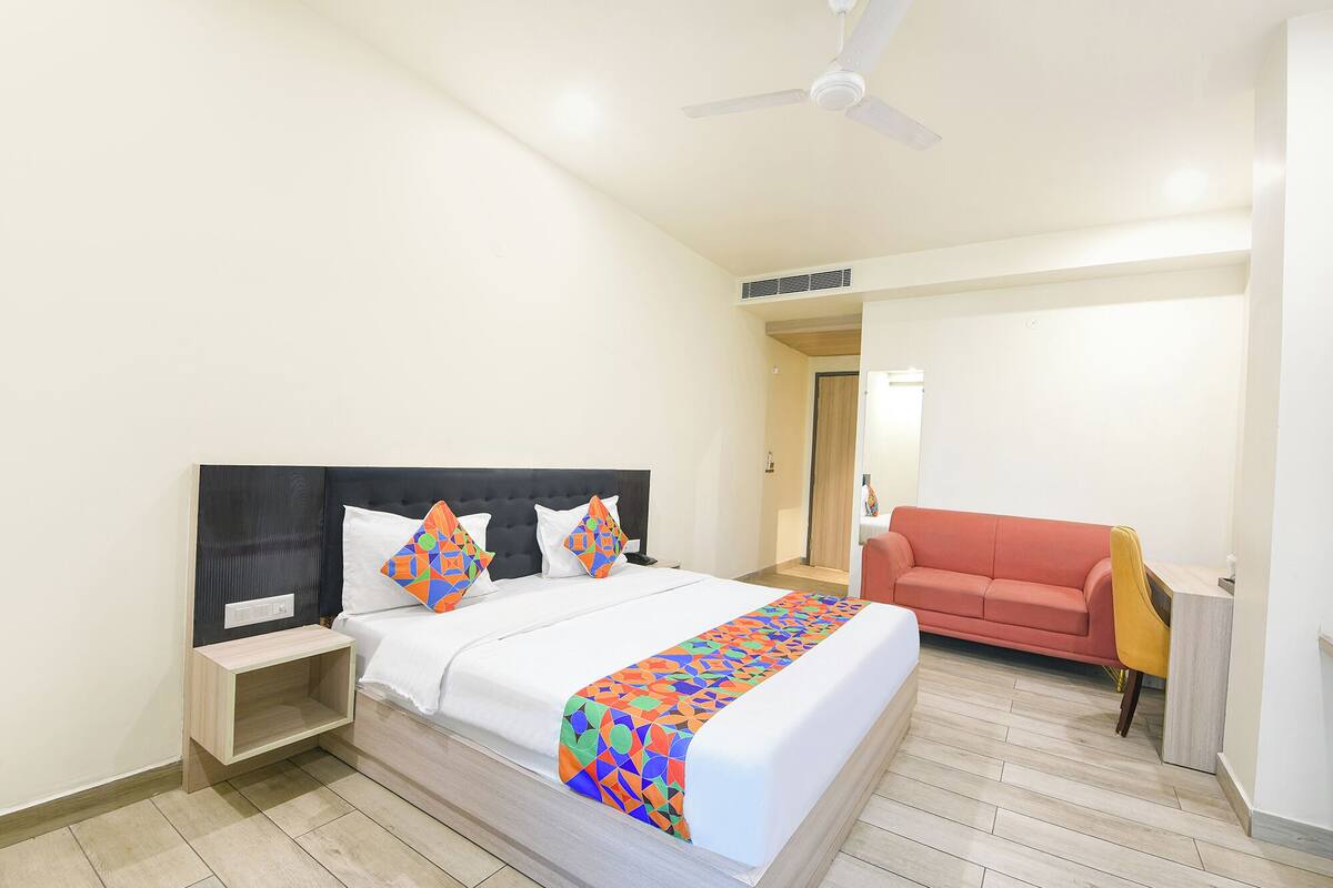 Habitación de hotel con cama, mesita de noche, sofá, ventilador de techo y puerta que da a otra habitación.