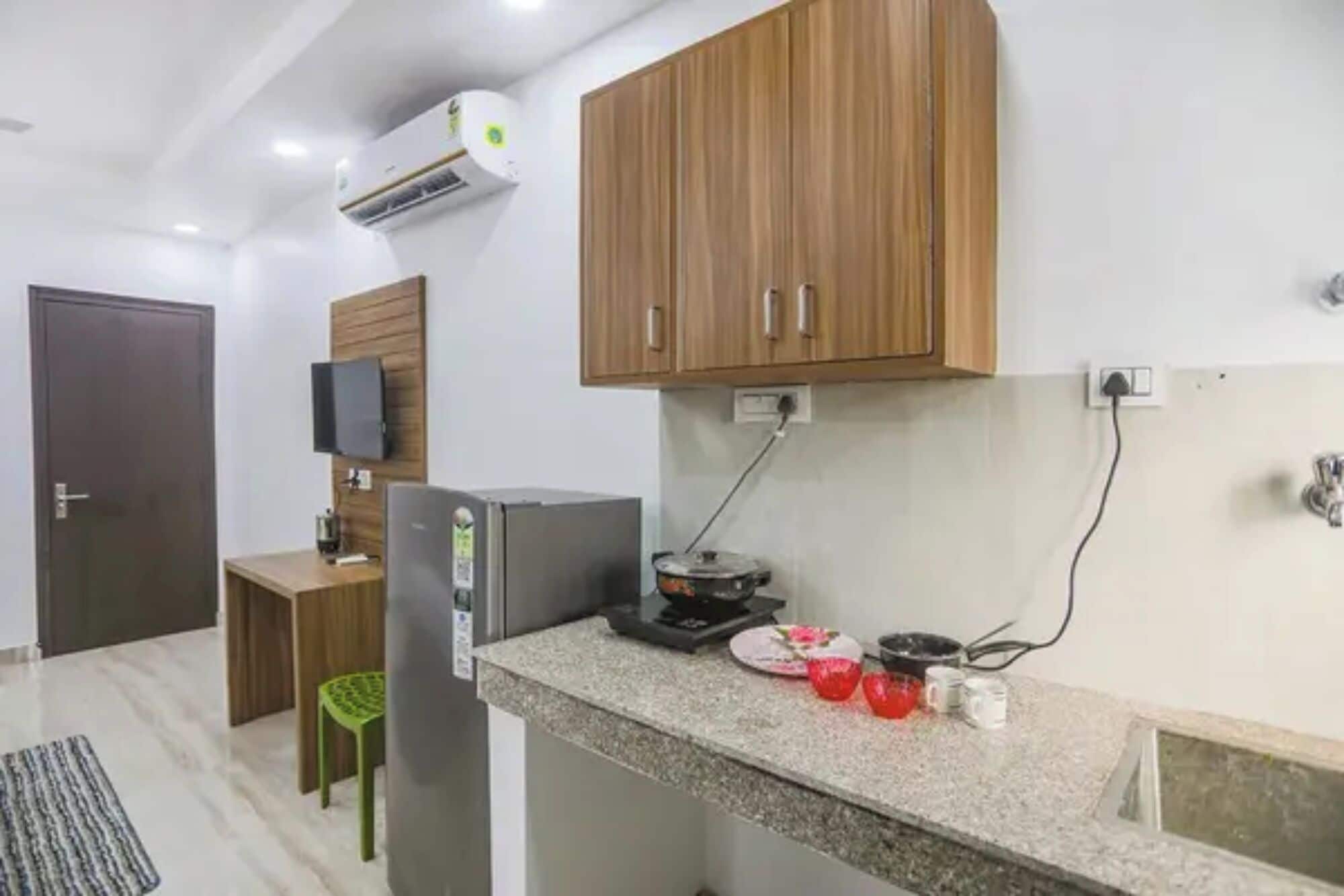 Une cuisine avec des meubles en bois, une cuisinière encastrée, un réfrigérateur et un téléviseur fixé au mur.
