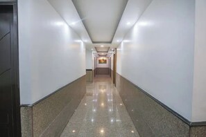 A long, narrow hallway with a polished floor, white walls, and a ceiling with recessed lighting. - Fabhotel Unique Stay (Noida)