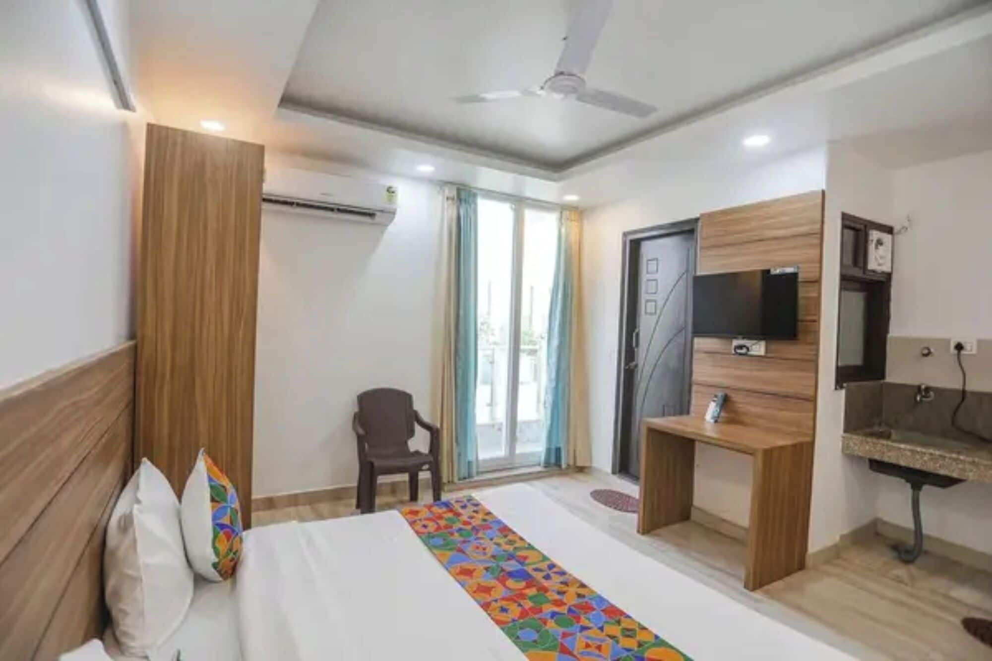 Una camera d'albergo con un letto, una scrivania, una sedia, una TV e una ventola a soffitto.