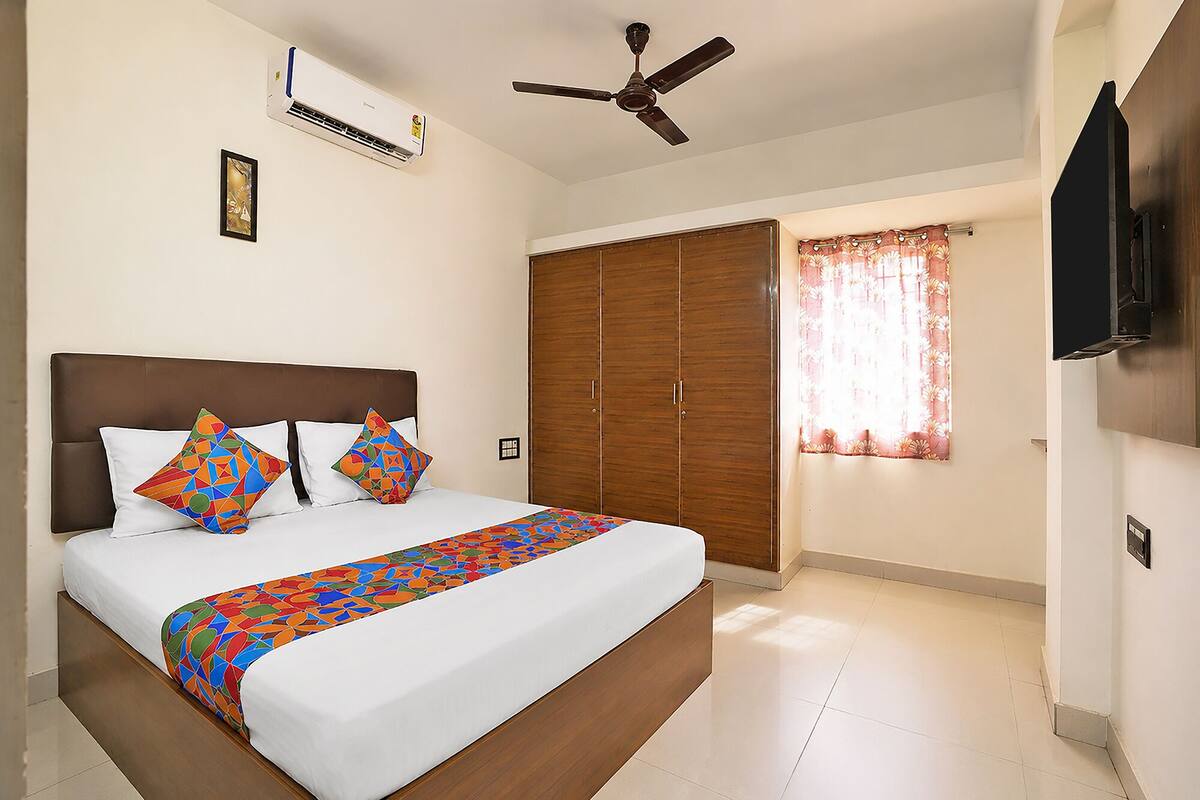 A bedroom with a bed, a ceiling fan, an air conditioning unit, a wardrobe, and a television.