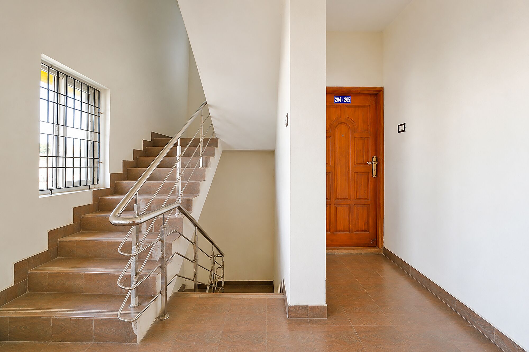 Una escalera con barandillas de metal, una puerta de madera y un ventanal con rejas.