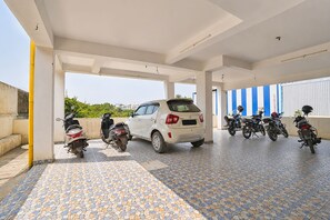 A covered parking area with a white car and several motorcycles parked. - Fabhotel V Inn Rooms (Chennai)