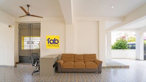 Un hall de hotel con mostrador de recepción, un sofá, un ventilador de techo y suelo de baldosas.