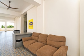 A hotel reception area with a sofa, a desk, and a ceiling fan.