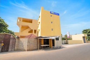 A modern building with a flat roof, a sign reading 'Tab Hotels,' and a gated entrance with a stone wall.
