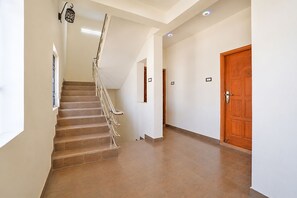 A staircase with a handrail, a wooden door, and a light fixture on the wall. - Fabhotel V Inn Rooms (Chennai)