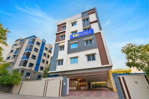 Um hotel com vários andares, um destaque para a placa 'fab hotels', uma entrada coberta e um acesso por portão.