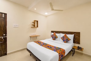Ein Hotelzimmer mit Bett, Nachttisch, Wandregal, Deckenventilator und Tür.