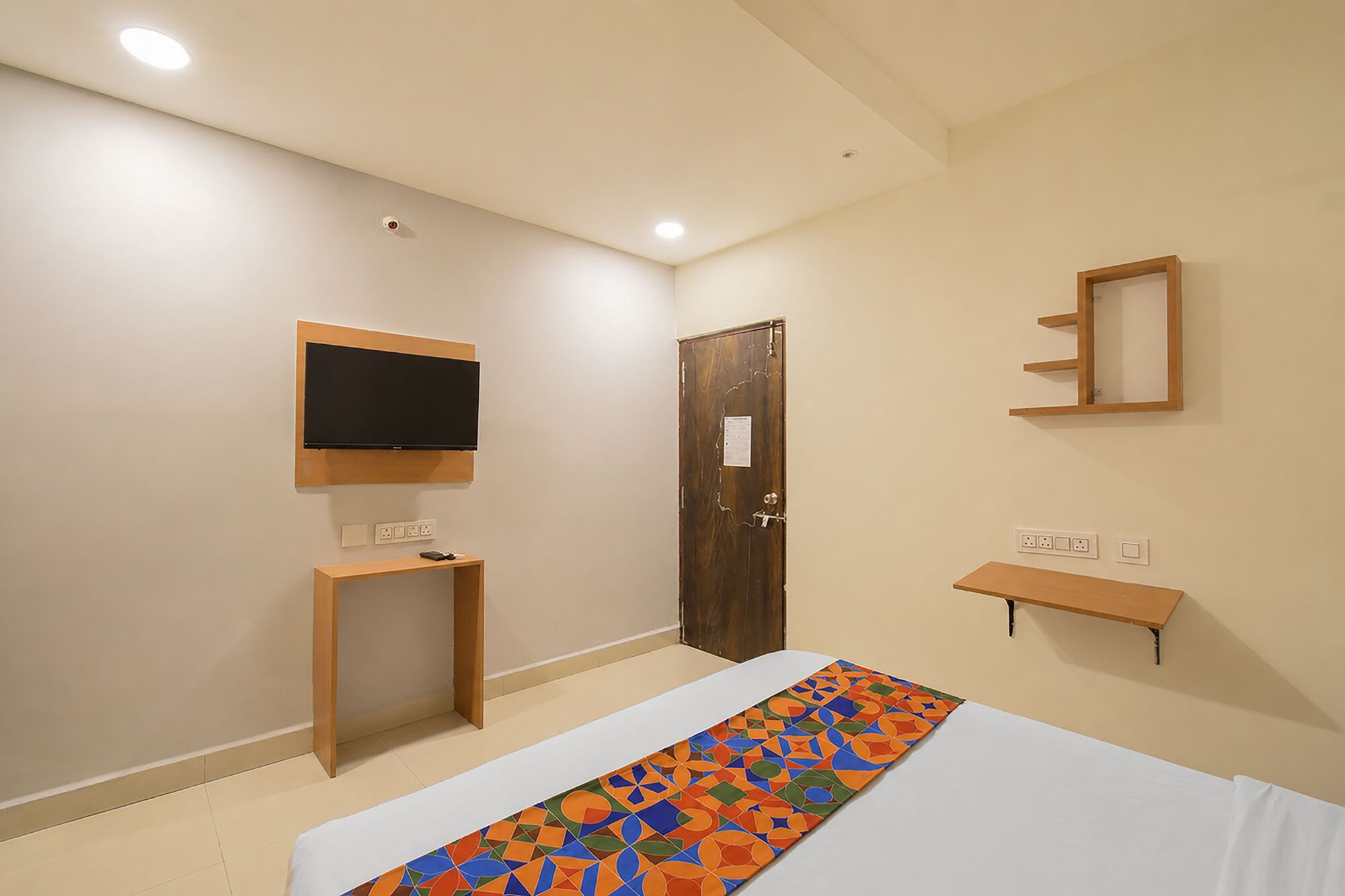 Une chambre à coucher avec un lit, un téléviseur fixé au mur, une porte et une petite table.