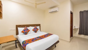 A bedroom with a bed, a ceiling fan, an air conditioning unit, a bedside table, and a bathroom with a sink and shower. - FabHotel White Ridge Kamineni - Nr. Saroornagar Indoor Stadium- L.B Nagar (Hyderabad)