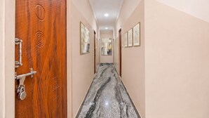 A hallway with a wooden door, marble floor, and framed artwork on the walls. - Fabhotel Whites Inn Vandalur (Chengalpattu)