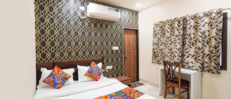 A hotel room with a bed, a desk, a chair, an air conditioning unit, and a window with curtains.
