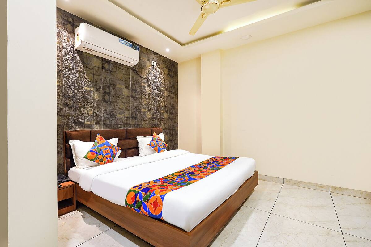 A hotel room with a bed, a nightstand, an air conditioning unit, and a ceiling fan.