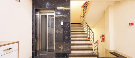 A modern interior with a marble staircase, a fire extinguisher, and a door leading to an elevator.