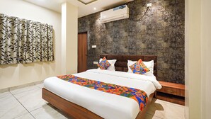 A bedroom with a bed, a nightstand, a wall-mounted air conditioner, and a patterned curtain. - FabHotel Zamzam Residency (Bhopal)